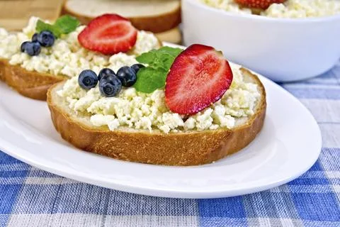 Slices of bread with curd cream, mint, blueberries and strawberries, a bowl of Stock Photos