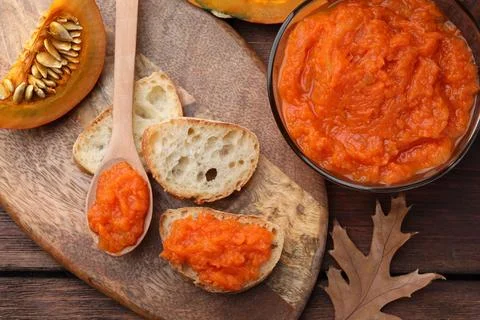 Slices of bread with delicious pumpkin jam and fresh pumpkin on wooden table Stock Photos