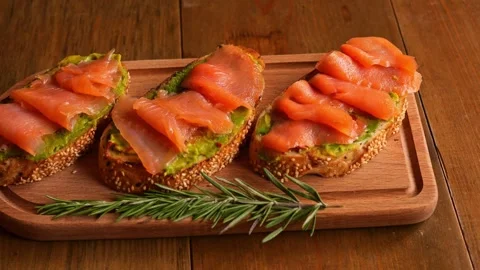 Slices of bread with red fish and avocado are presented on table Avocado Stock Footage 265630973