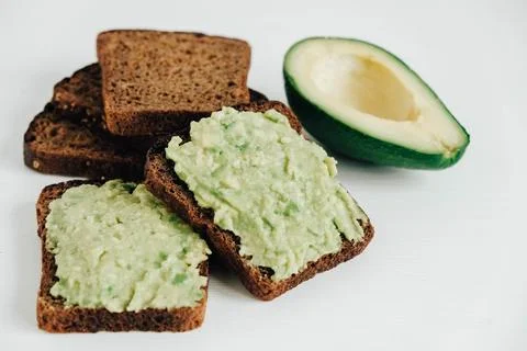 Slices of brown bread with avocado on a white wooden table. Copy, empty spa.. Stock Photos