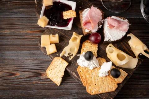 Slices of cheese, cracker, ham, jam, grapes, olives, on a dark wooden backgro Foto stock