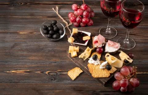 Slices of cheese, cracker, ham, jam, grapes, olives, 2 glasses of red wine on Stock Photos