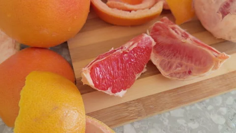 Slices of fresh red grapefruit and its peel are placed on a wooden cutting board Stock Footage 330794634