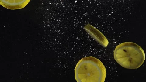 Slices of lemon dropped in water with splash and air bubbles isolated over black Stock Footage 293086205