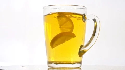Slices of lemon falling into glass of tea on white background slow motion Stock Footage 122010966