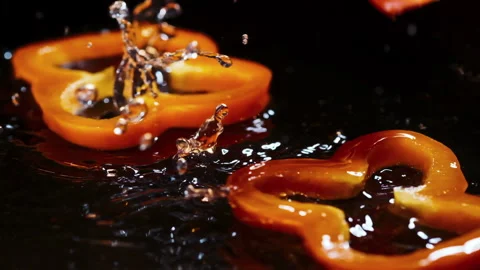 Slices of orandge bell pepper fall down on brown wooden board with water drops Stock Footage 154428341