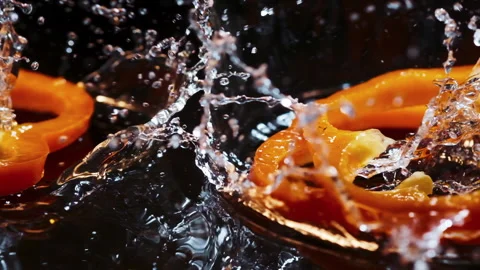 Slices of orandge bell pepper fall down on brown wooden board with water drops. 動画素材 155239752