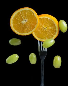 Slices of oranges on a fork surrounded by grapes Stock Photos
