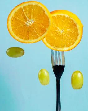 Slices of oranges on a fork surrounded by grapes Stock Photos