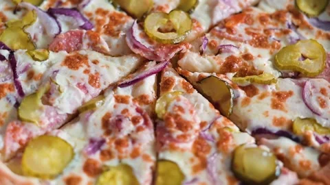 Slices of pizza are arranged on a surface, topped with pickles and red onion. Stockbeeldmateriaal 338290125