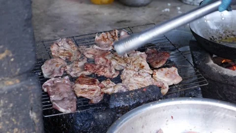 Slices of pork cook on wire mesh above red-hot coals, showcasing authentic Stock-Footage 313485943