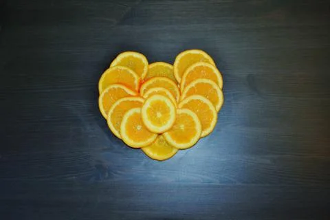 Slices of ripe oranges posed in a shape of a heart on background. Stock Photos