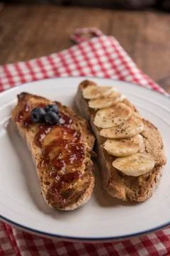 Slices of rustic bread with peanut butter, banana and strawberry jam Stock Photos