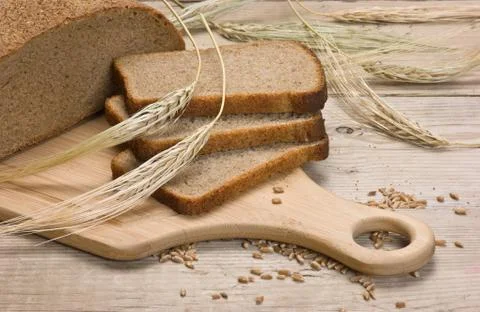 Slices of rye bread and ears of corn on a wooden table Stock Photos