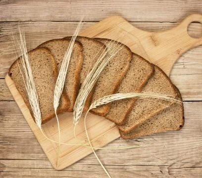 Slices of rye bread and ears of corn on the wooden table 스톡 사진