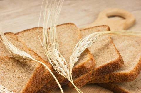 Slices of rye bread and ears of corn on the wooden table Stock Photos