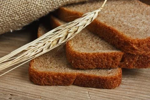 Slices of rye bread and ears of corn on a wooden table Foto stock