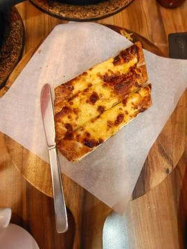 Slices of toasted cheesy garlic bread on parchment paper with a butter knife. Stock Photos