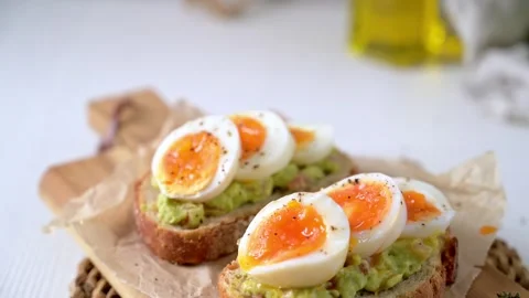 Slices of Toasted Sourdough Bread with Mashed Avocado and Soft Boiled Egg Stock Footage 330689923