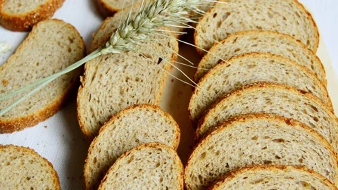 Slices of whole grain bread arranged on a white surface with a stalk of wheat Stock Footage 336322824