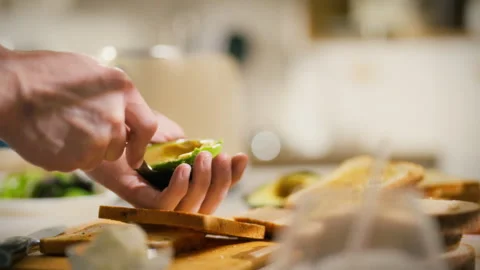Slicing and preparing fresh avocado for a sandwich in a cozy kitchen setting Stock Footage 323932087
