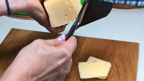 Slicing cheese into thin cuts with a cheese slicer on a cutting board – close-up Stock Footage 314734434
