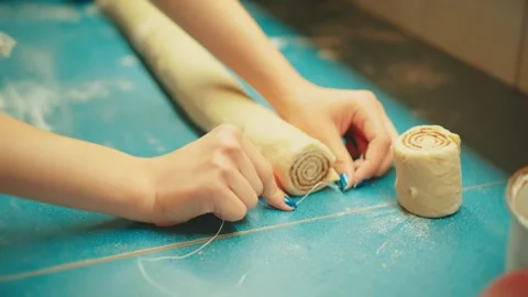 Slicing cinnamon roll dough log, close up of teenager cutting raw pastry. Stock Footage 332751452