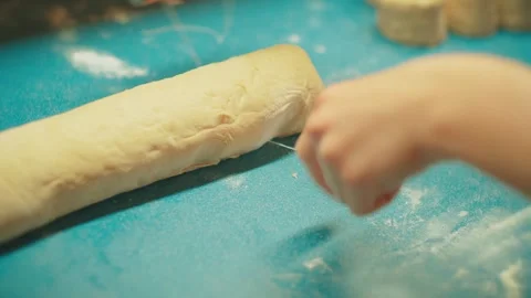 Slicing cinnamon roll dough log, close up of teenager cutting raw pastry. Stock Footage 332751914