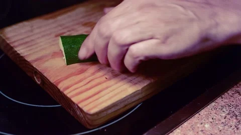 Slicing cucumber into thin slices on a wooden board to cook a vegan meal Stock Footage