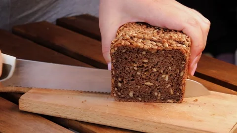 Slicing dark whole grain bread with sunflower seeds on wooden cutting board.. Stock Footage 313553322