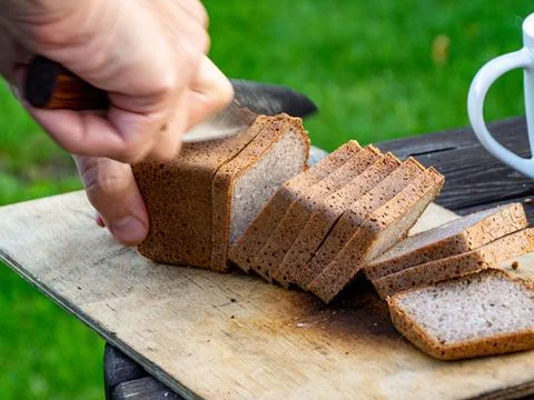 Slicing dense rye bread loaf on rustic cutting board with natural daylight Stock Photos