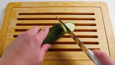 Slicing fresh cucumbers on a cutting board at the kitchen table. Stock Footage 230739934