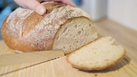 Slicing a Freshly Baked Artisan Bread Loaf on a Wooden Cutting Board for Stock Footage 295515936