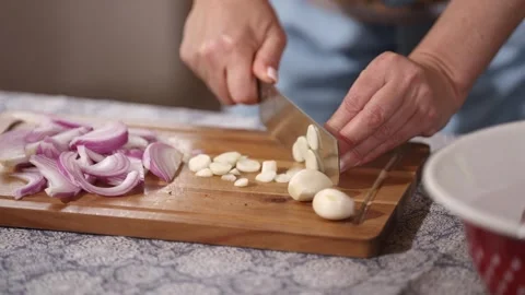Slicing Garlic and Red Onion on Wooden Cutting Board for Homemade Cooking Stock Footage 340555216