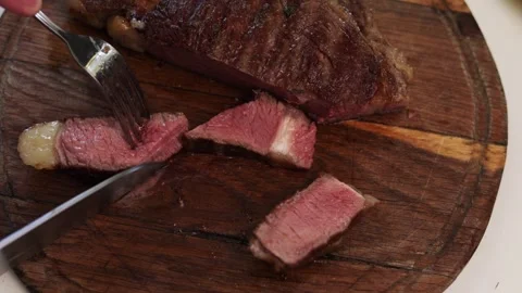Slicing juicy medium-rare steak on a rustic wooden board with a knife Stock Footage 340563433