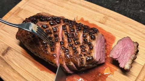 Slicing medium-rare duck breast with golden crust on a wooden cutting board Stock Footage 304692537