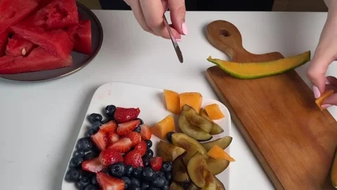 Slicing melon and removing rind, placing fruit pieces on plate with strawberries Stock Footage 316675032
