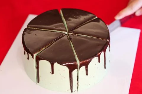 Slicing a Mint Chocolate Drip Cake on Red Background Фото