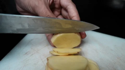 Slicing a Potato on Cutting Board, Close-up of hands slicing a peeled potat.. 動画素材 304978608