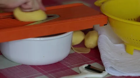 Slicing potatoes with an orange mandoline slicer into a bowl Stock Footage 346030644