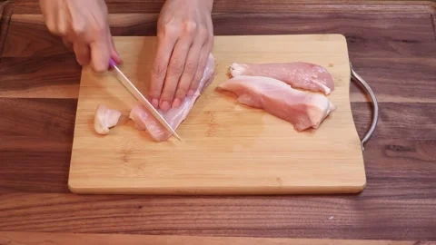 Slicing Raw Chicken Breast Into Large Pieces on Wooden Cutting Board Stock Footage 334811159