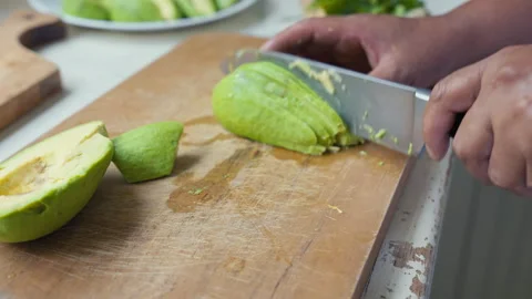 Slicing ripe avocado into thin wedges on a wooden cutting board. Stock Footage 338341479