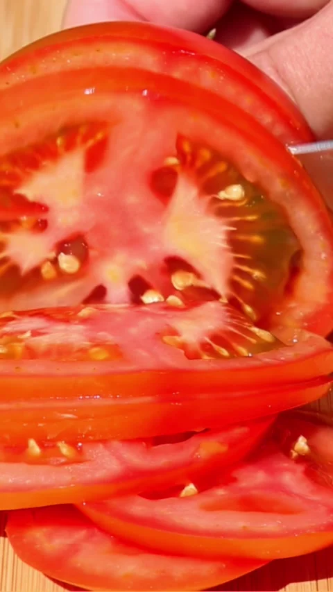 Slicing ripe tomato into thin fresh slices on wooden board Video stock 316378948