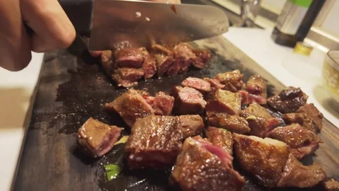 Slicing Seared Beef Strips into Pieces on a Wooden Cutting Board Stock Footage 344670080
