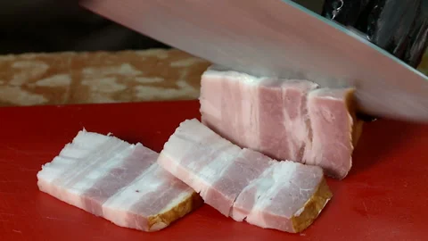 Slicing slices of bacon on a plastic board with a cook knife Stock Footage 121913301