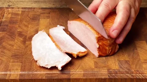 Slicing smoked meat into thin pieces on a wooden cutting board in the kitchen Stock Footage 325032459