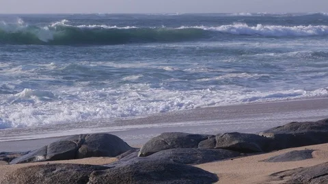 Slide left on sandy beach as choppy white waves crash against rocks Video stock 105164707