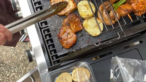 Slide left top view of man using tongs to turn fresh and juicy meat on BBQ grill Stock Footage 136735926