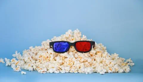 A slide of popcorn on a blue background and 3D glasses. Stock Photos