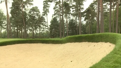 Slide right to left past a golf bunker as a greens keeper mows the green Stock Footage 80468386